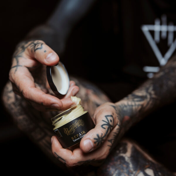 Unmistakable - Vegane Premium Tattoopflege - Tätowierte Hand entnimmt Creme aus Repair Tattoo Creme
