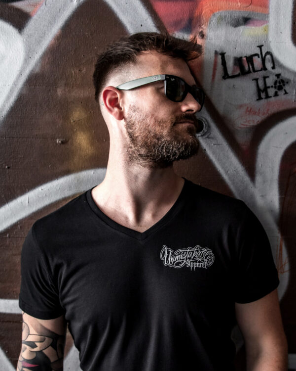 Unmistakable - V-Neck-Shirt - Junger Mann mit Bart lehnt an Wand