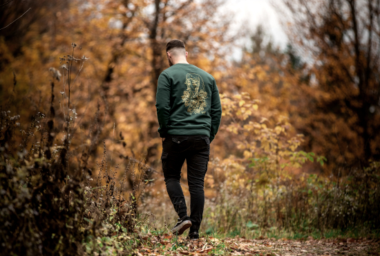 Unmistakable Apparel - Tattoo clothes for men - junger Mann mit grünem Pullover in Wald