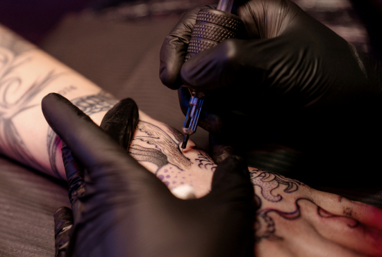 Unmistakable - Nachhaltiger Tattoobedarf - Nahaufnahme von Händen in schwarzen Handschuhen, die Handrücken tätowieren