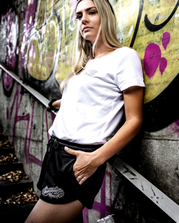 Unmistakable Sweatshort - Schwarz für Frauen - Junge. blonde Frau lehnt an Graffiti-Wand